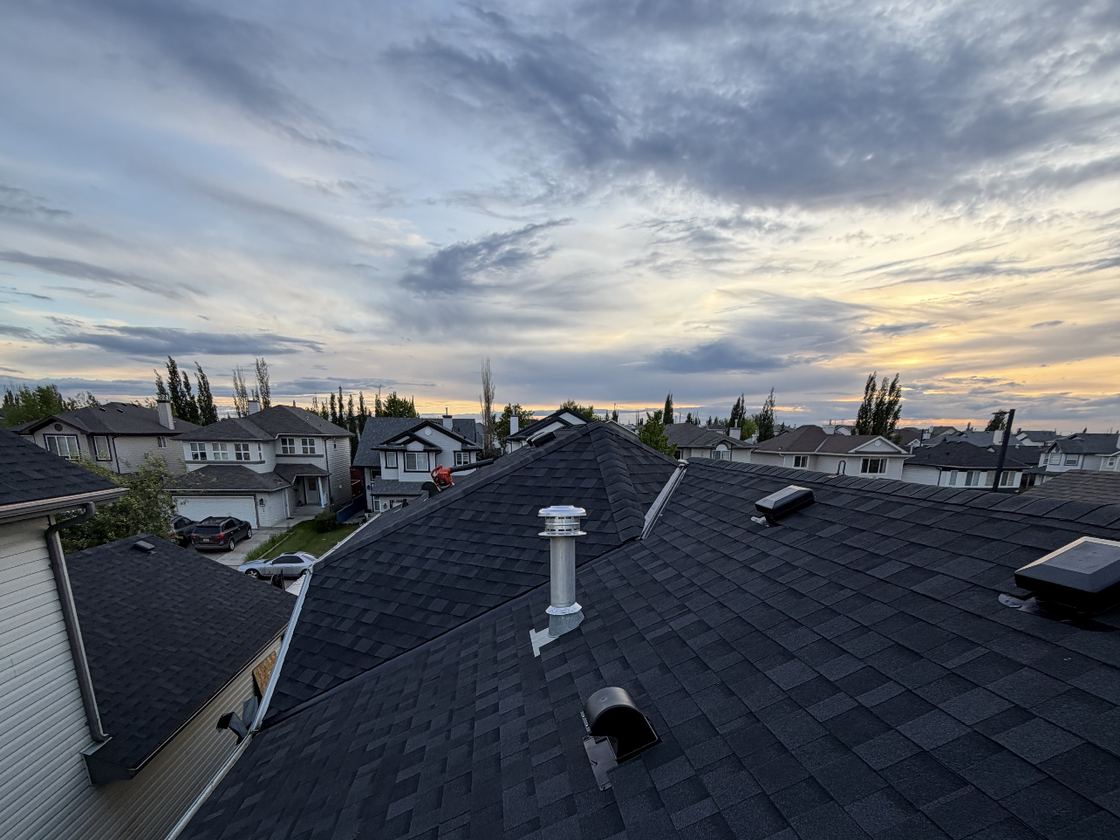 A completed SureSky asphalt shingle roof at dusk, looking across the ridge and vents to an Alberta neighbourhood skyline